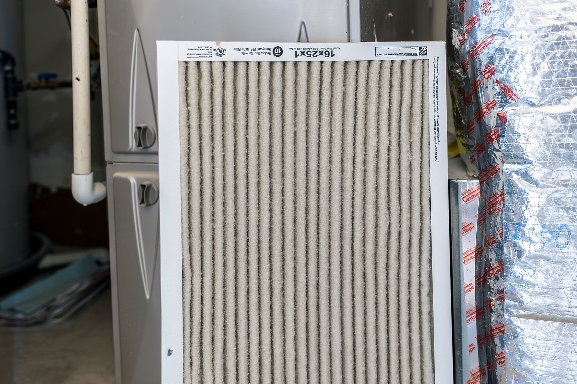 A dirty air filter is sitting next to a heater in a basement.