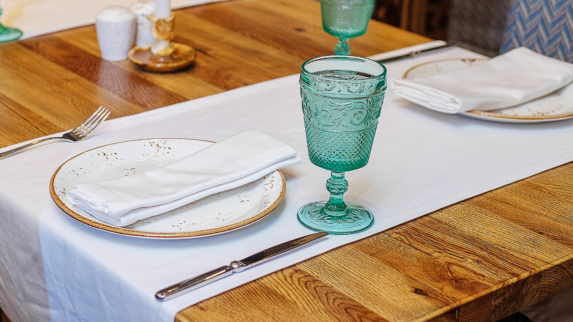 A wooden table with plates , utensils , and a green wine glass on it.