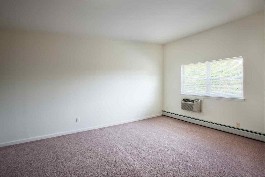 A carpeted bedroom with a window and an air conditioning unit