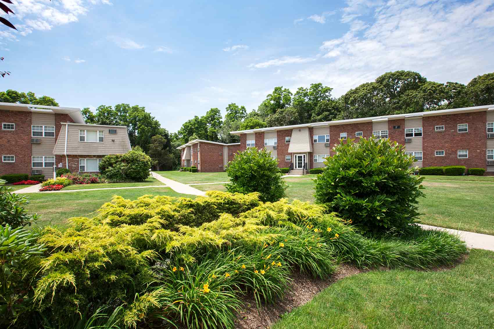 Landscaping and green grass with sidewalks leading to at least three apartment buildings, each with two stories