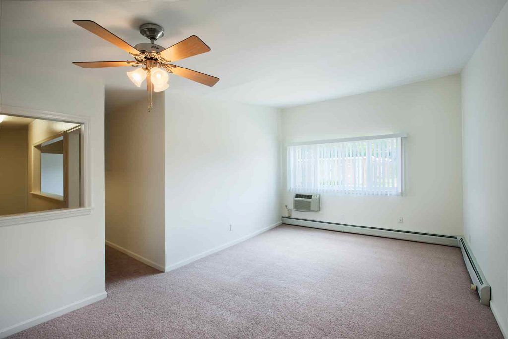 Carpeted living room area with air conditioning unit under window and a ceiling fan