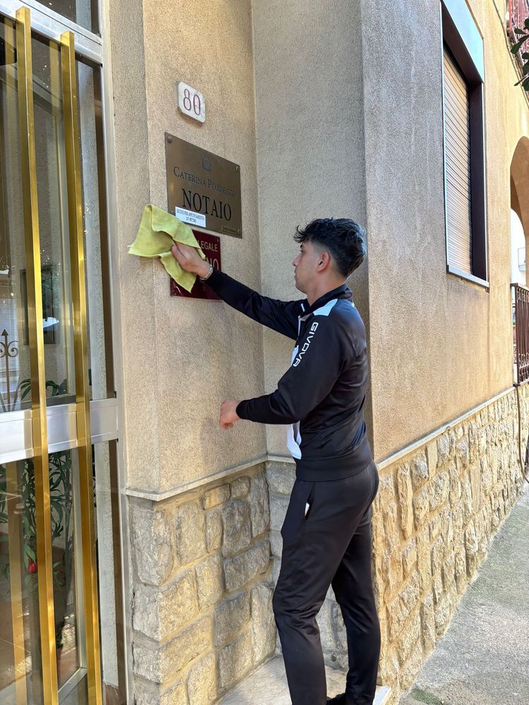 Una persona in tuta nera pulisce un cartello con un panno giallo sulla facciata di un edificio.