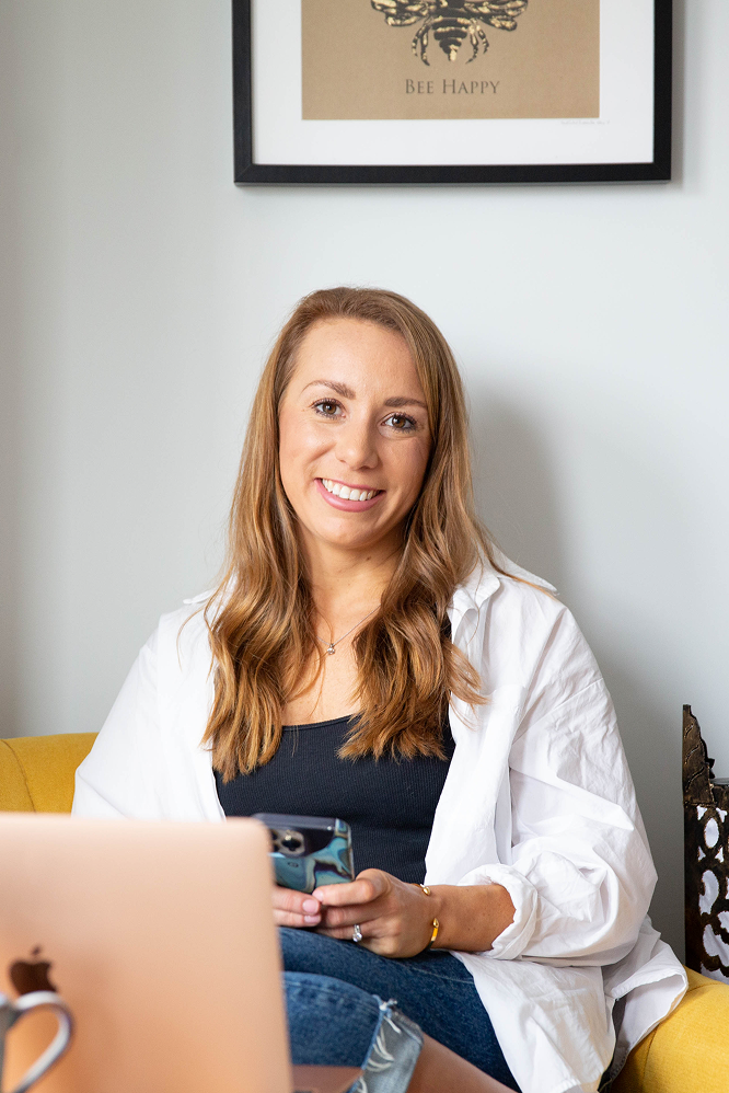 A woman is sitting on a couch with a laptop and a cup of coffee.