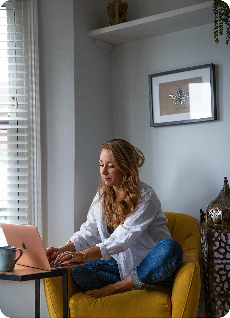 A woman is sitting in a yellow chair using a laptop computer.