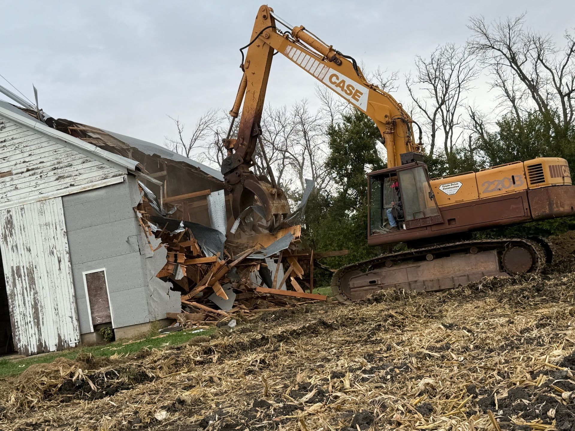 A yellow excavator is working on a pile of rocks in front of a building.