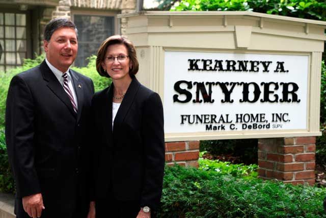 a man and a woman are standing in front of a funeral home sign .