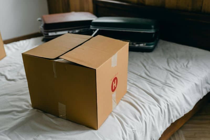 A cardboard box is sitting on a bed next to a suitcase.