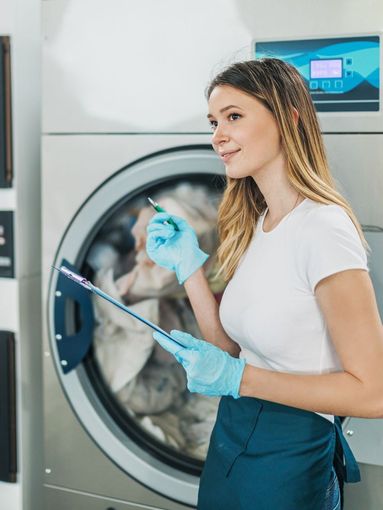 A woman is standing in front of a washing machine holding a clipboard.