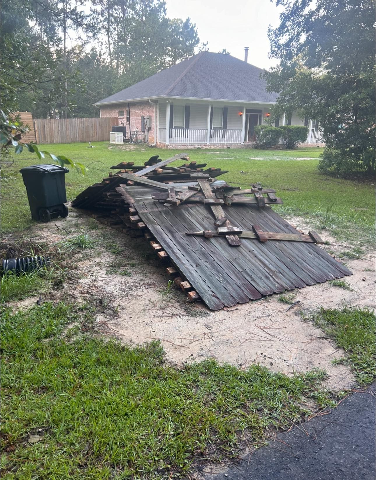 A pile of wood is sitting in the grass in front of a house.