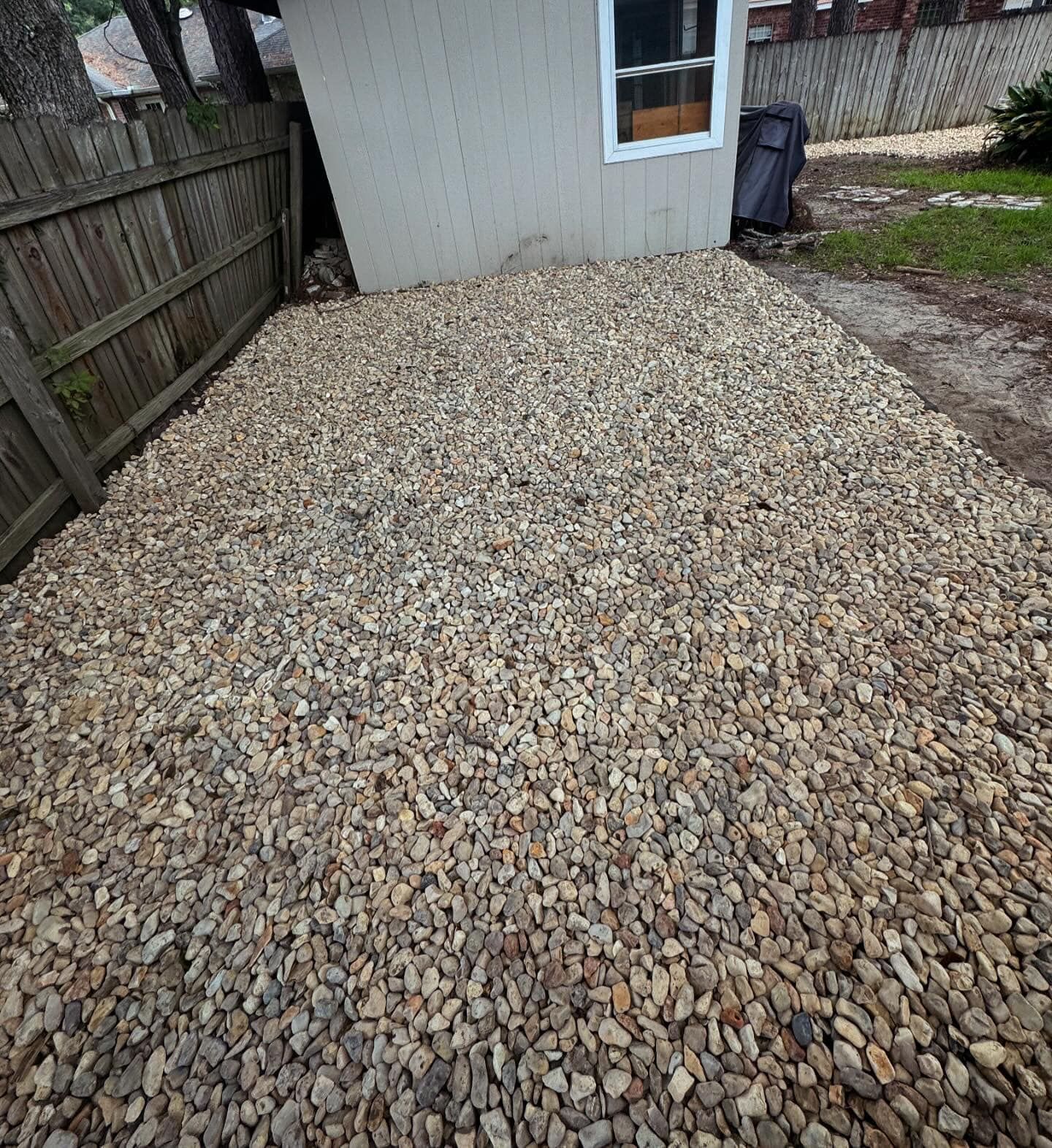 A gravel driveway in front of a house with a wooden fence.