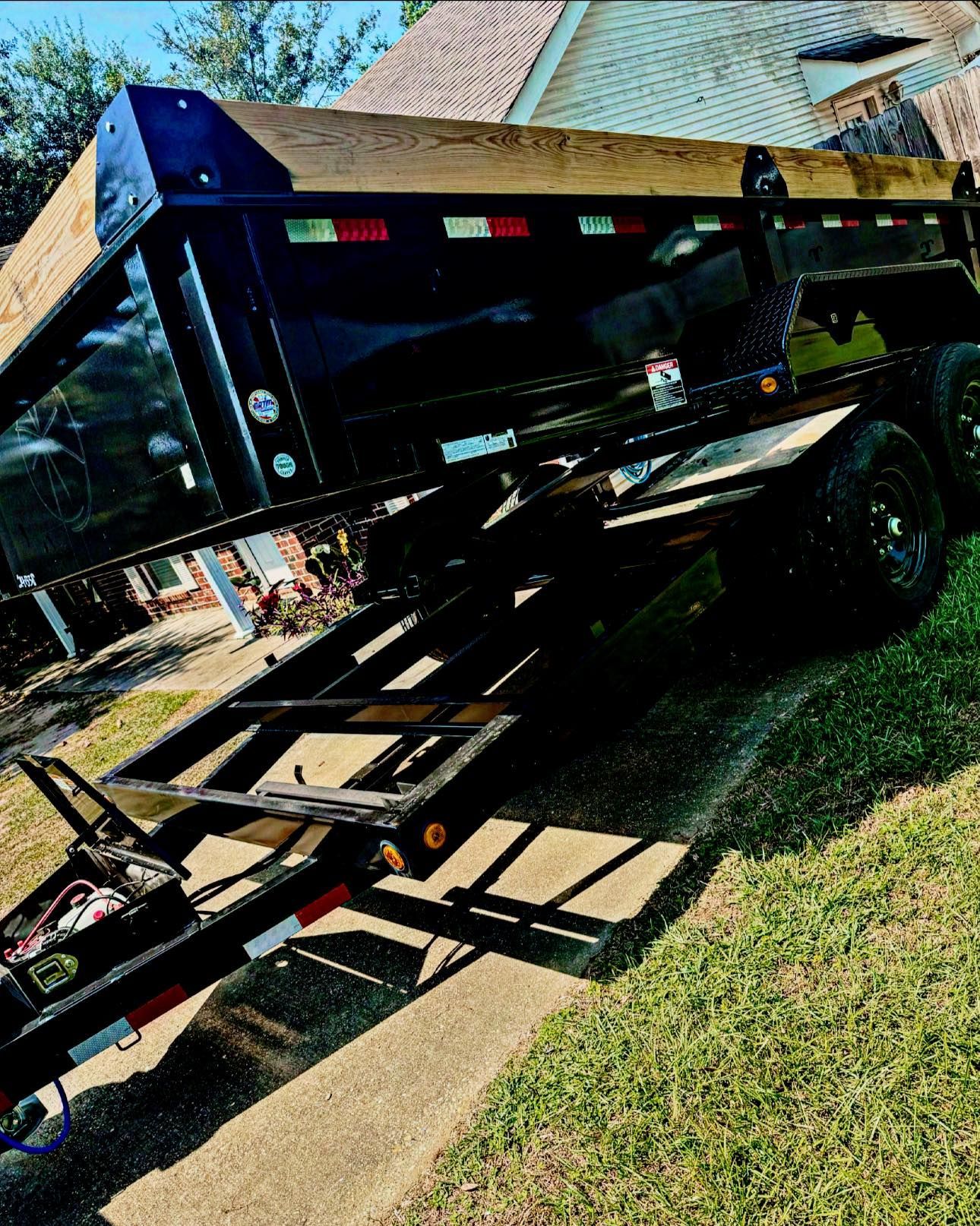 A dump trailer is parked on the side of the road in front of a house.