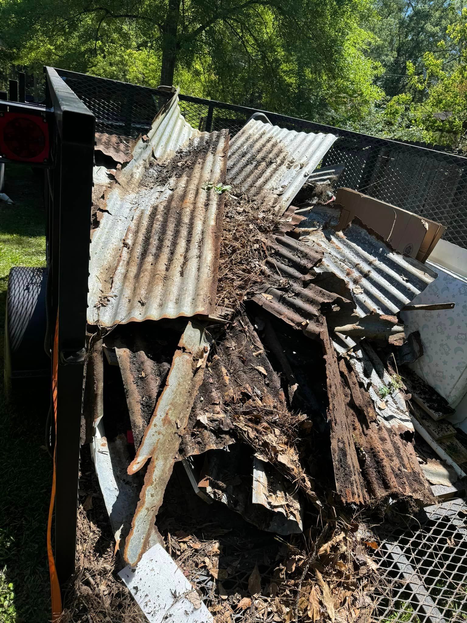 A trailer is sitting in the grass next to a pile of wood.