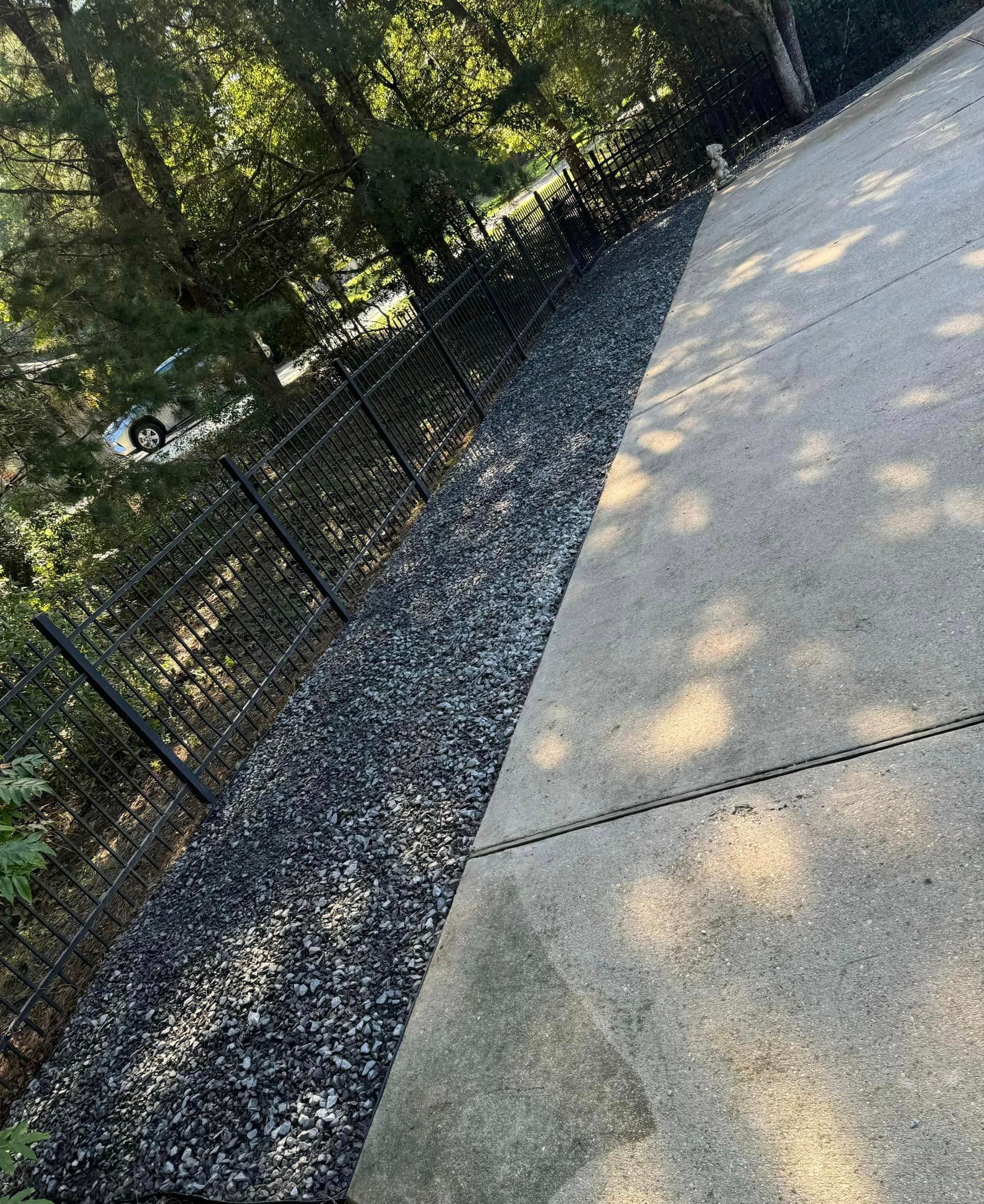 A concrete driveway with a chain link fence and trees in the background.