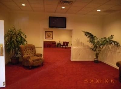 Interior with red carpet, armchair, plants, doorway to seating, a framed picture, and a television.