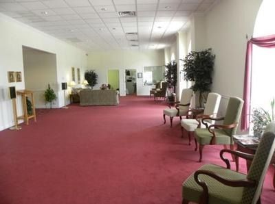 Spacious room with red carpet, chairs, and plants. Several doors and windows. Likely a waiting or reception area.