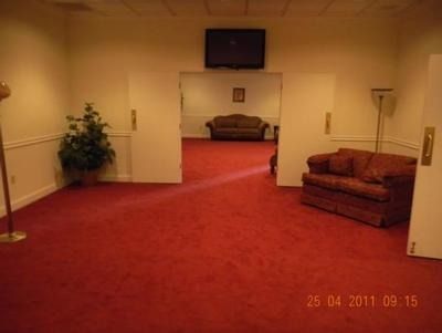 Empty room with red carpet, two couches, and a TV; doors lead to a similar room.