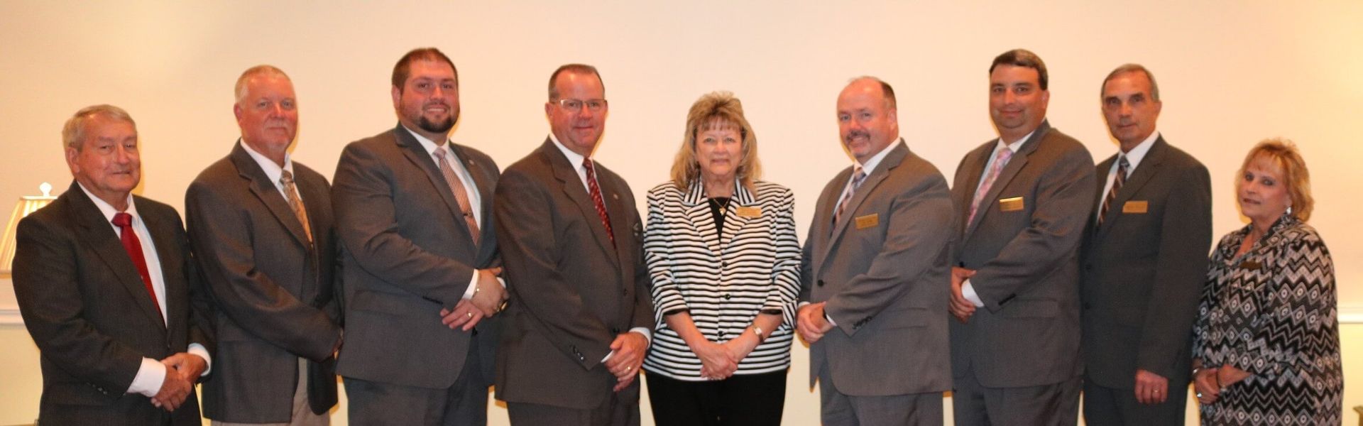 A group of ten people, most in suits, stand in front of a white wall.