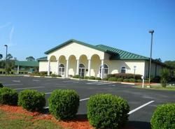 Building with arched columns, green roof, and parking lot on a sunny day.