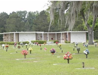 Cemetery with a long, light-colored building in the background and colorful artificial flowers on the graves.