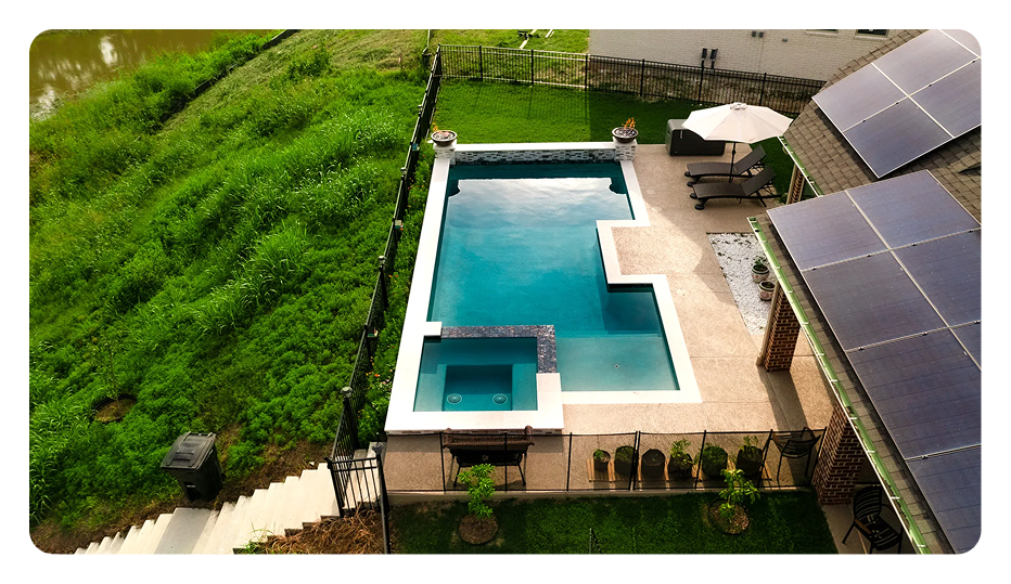 Aerial view of a rectangular swimming pool with a connected spa, surrounded by a patio, lawn, and solar panels.