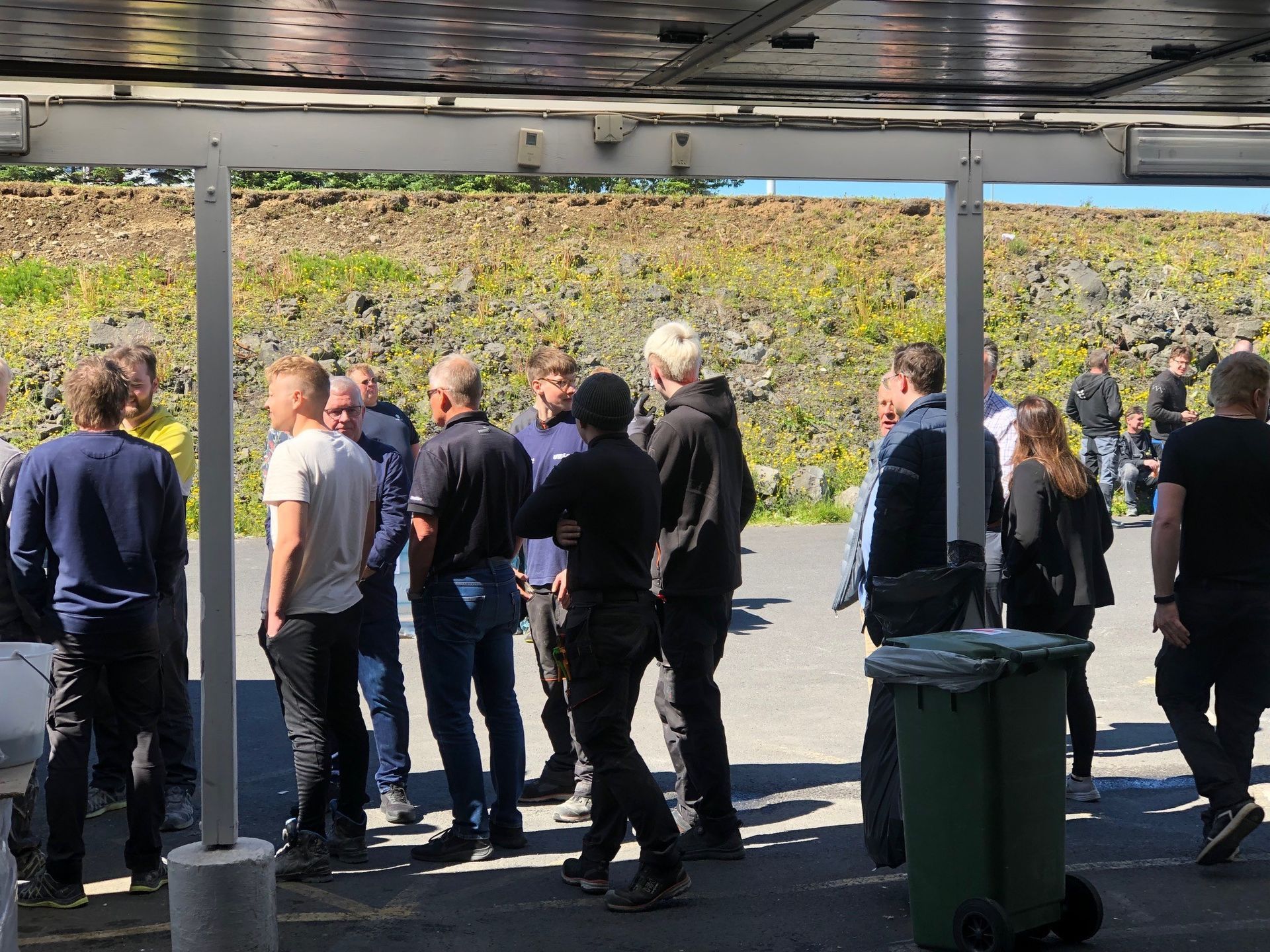 Hópur fólks stendur undir tjaldhimnu að tala saman.