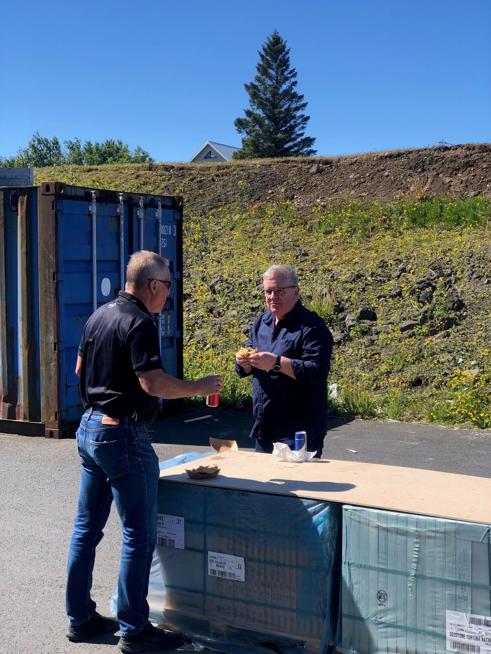 Tveir menn standa við hlið hvors annars fyrir framan bláan gám.