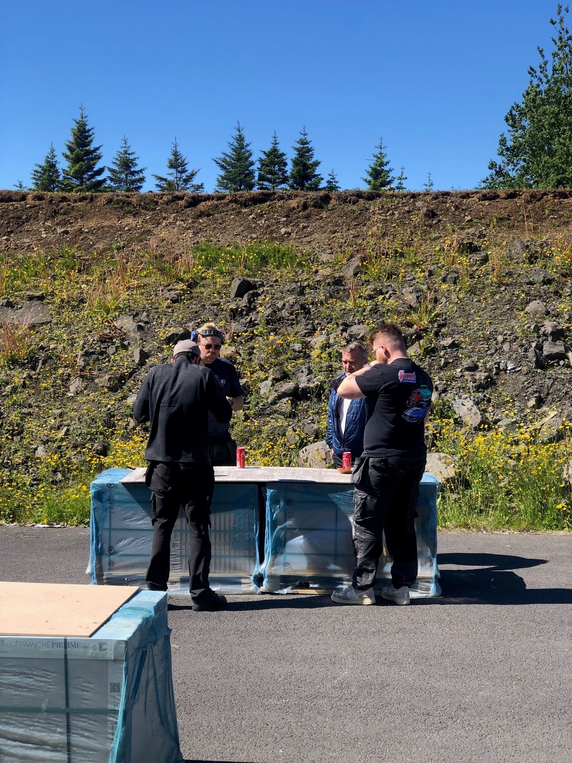 Hópur manna stendur í kringum borð á túni.