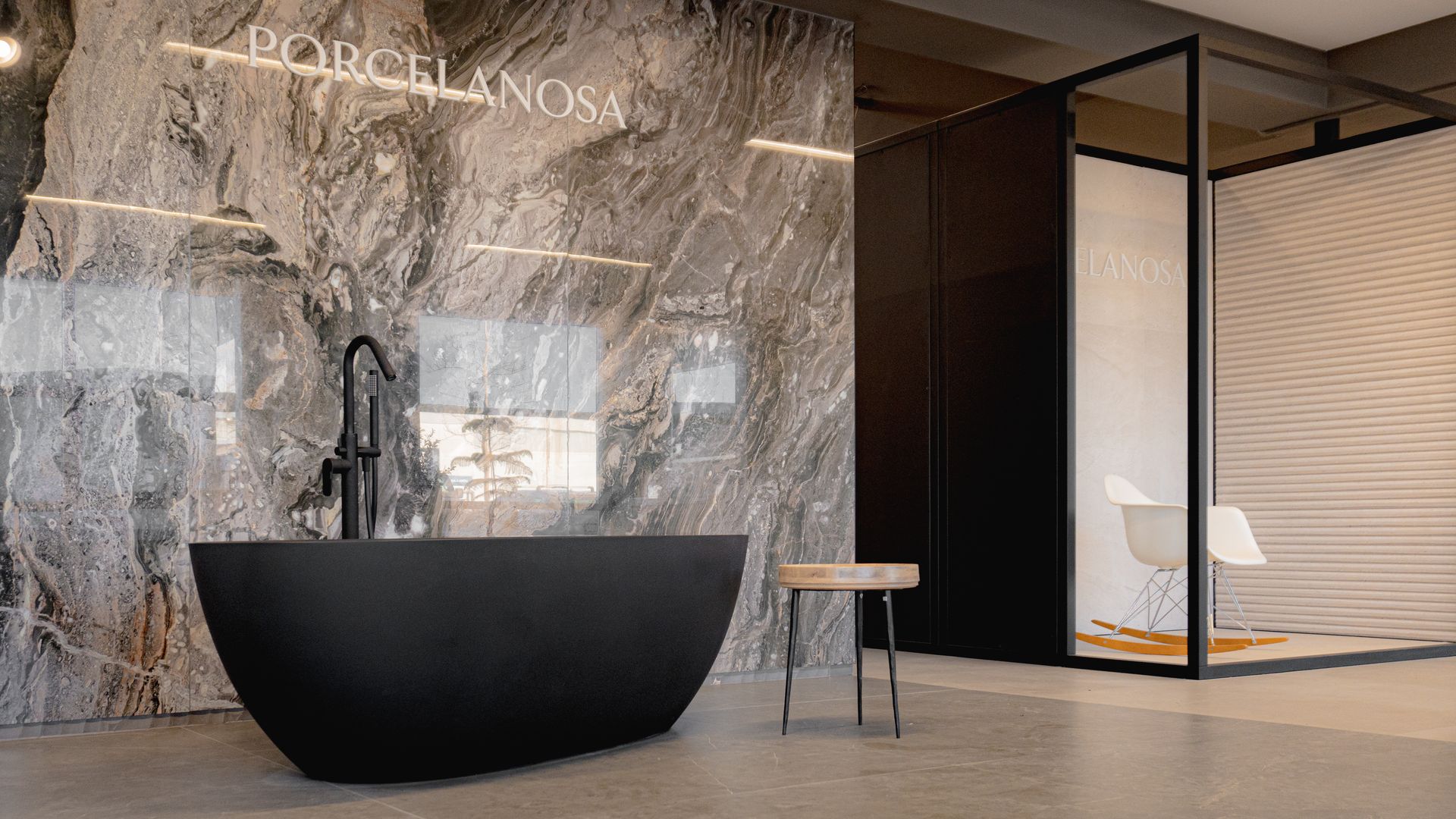 Svart baðkar situr á baðherbergi við hlið marmaravegg.