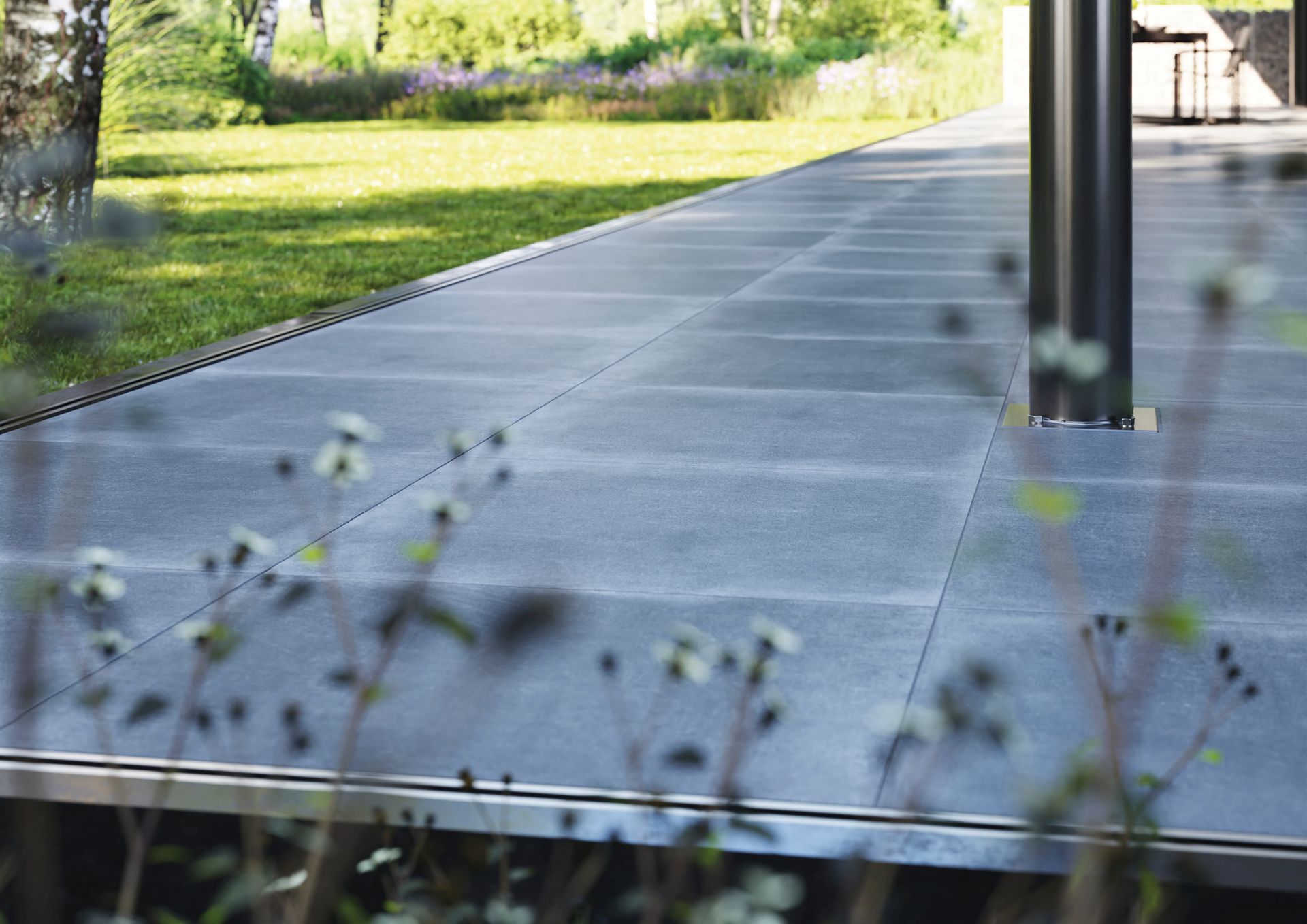 Steypt gangbraut sem liggur að gróskumiklum velli.