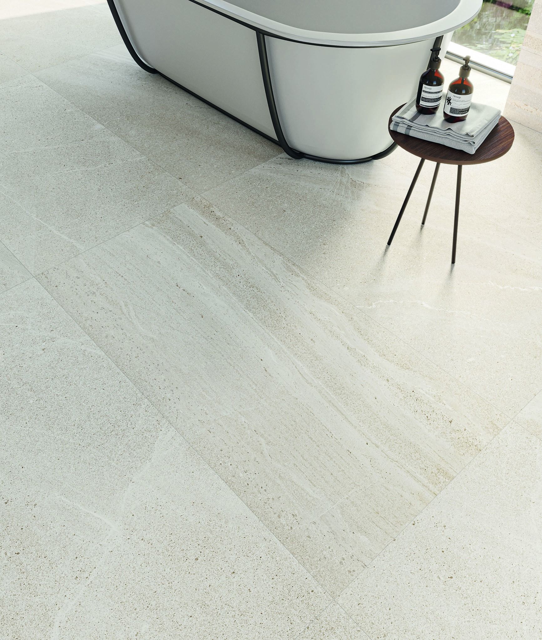 Baðkar situr á flísum á gólfi við hlið lítið borð.