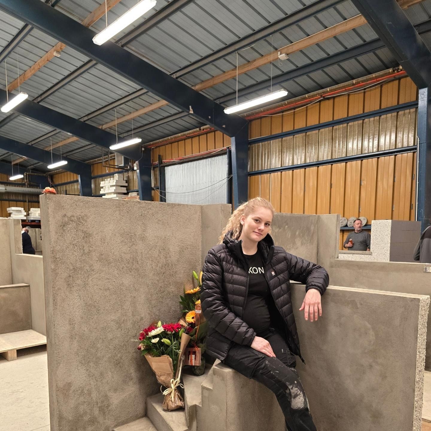 Kona situr á vegg með blómvönd fyrir framan sig