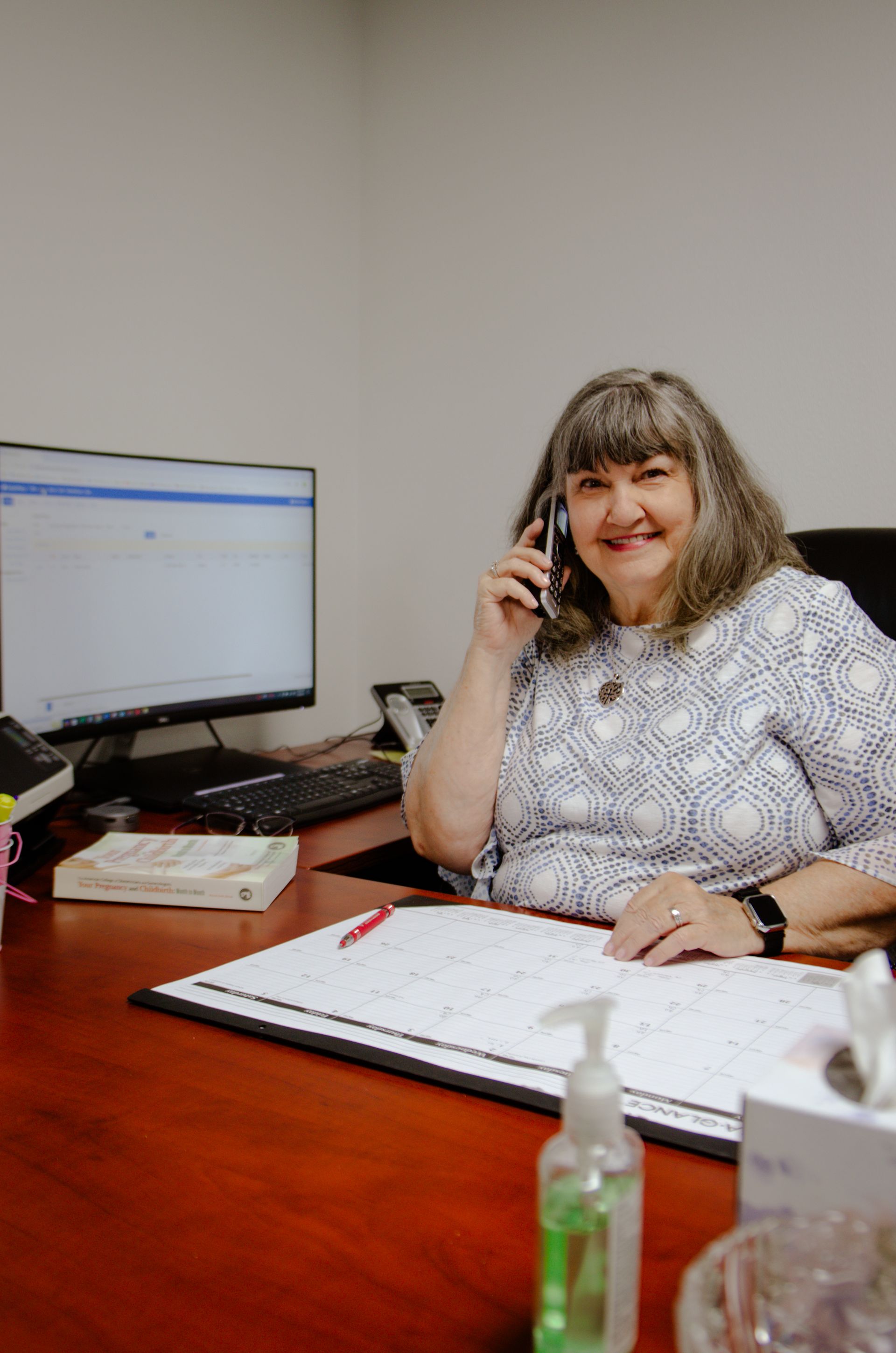 A woman is sitting at a desk talking on a cell phone.