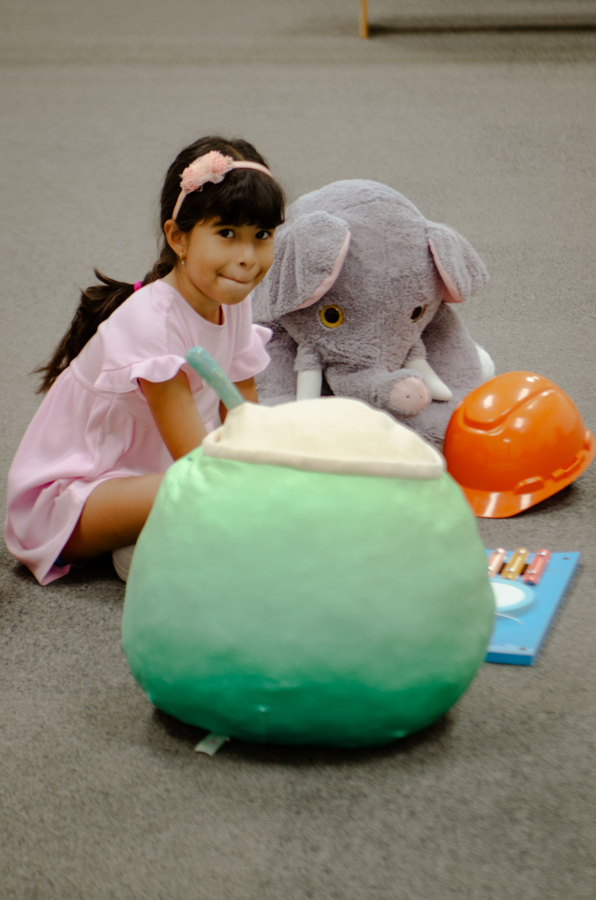 A little girl is sitting on the floor next to a stuffed elephant.