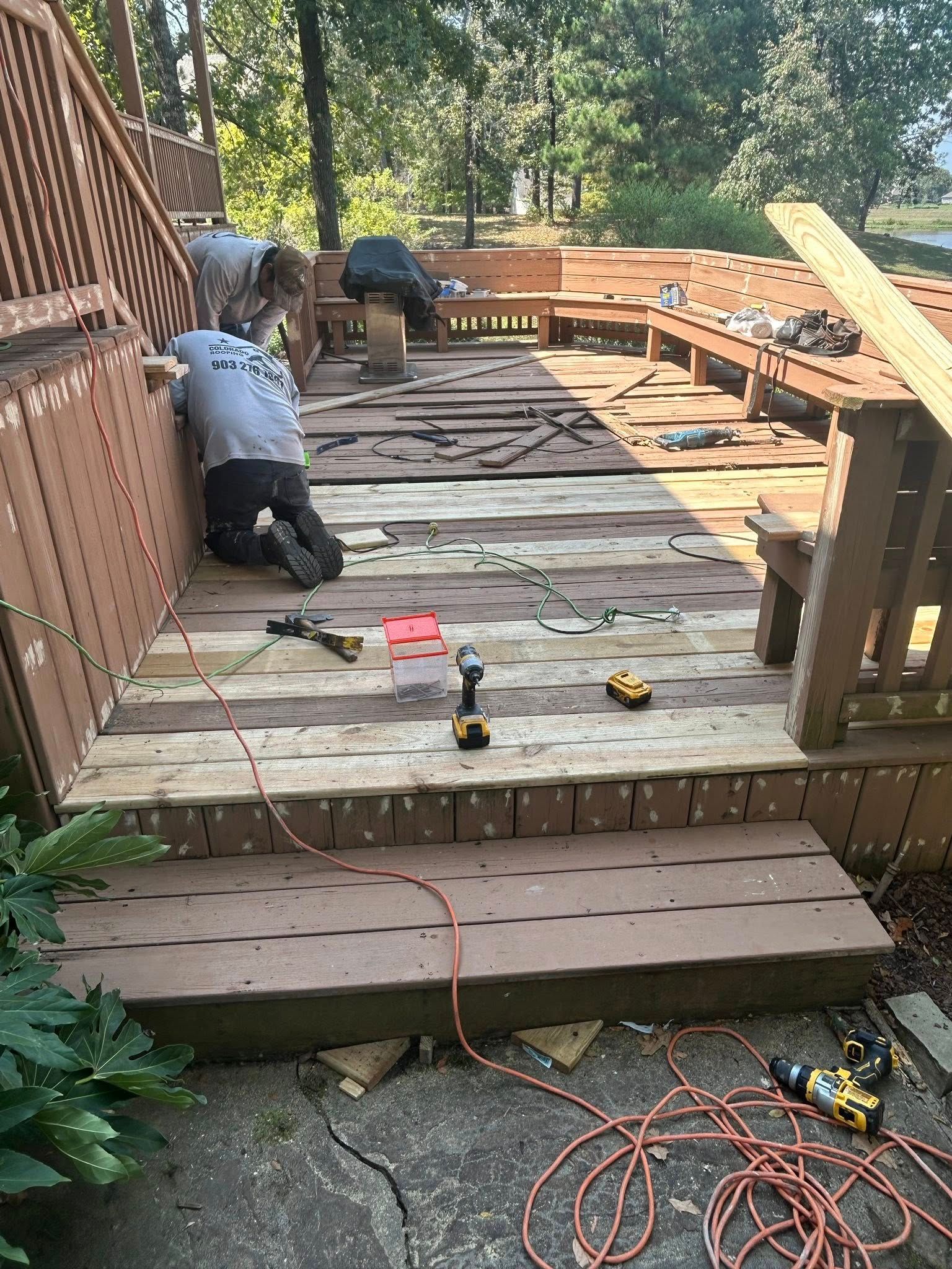 Workers renovating a wooden deck, removing boards and working with power tools outdoors.