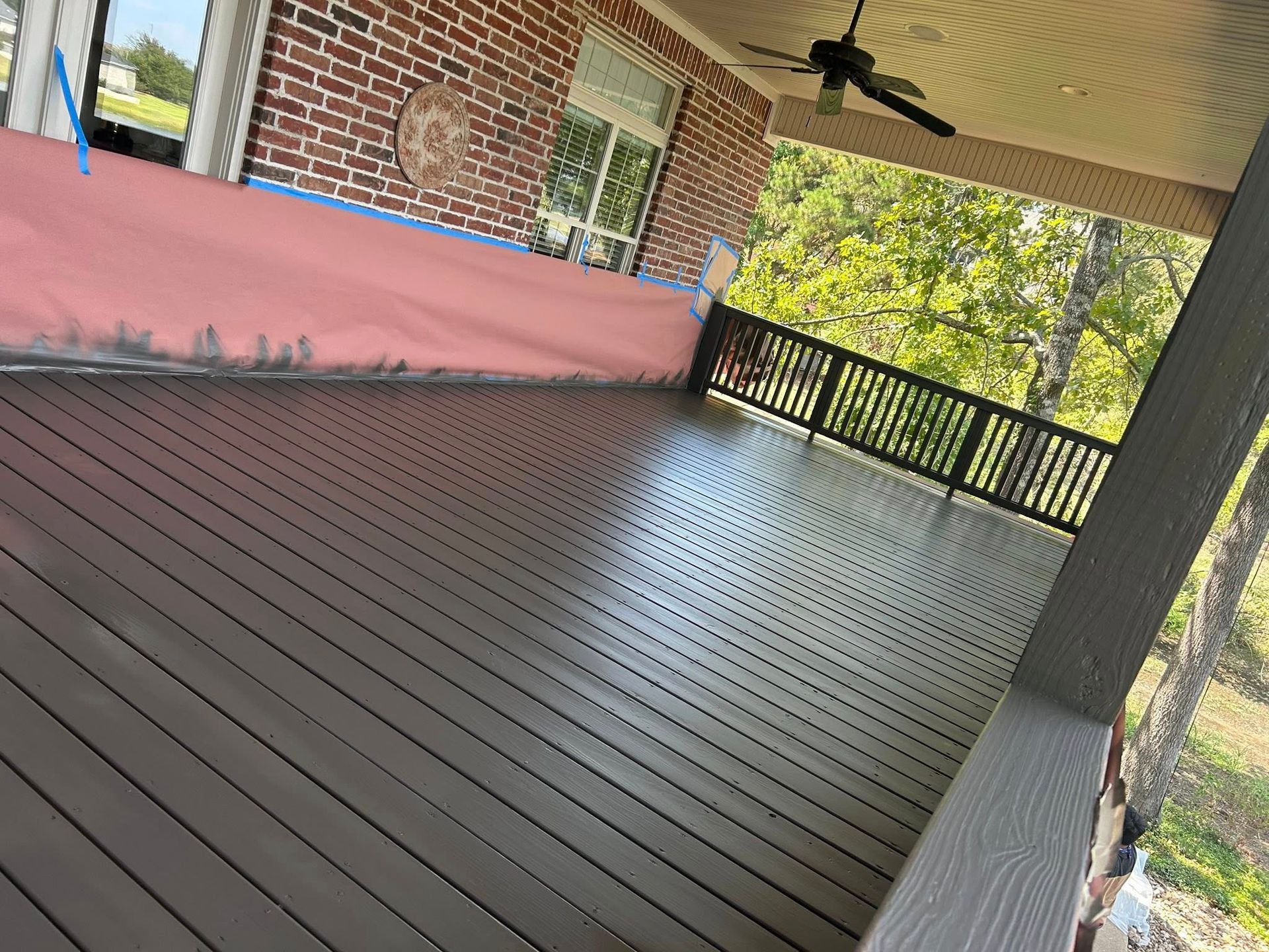A newly constructed brown composite deck on a porch with dark brown railings, a ceiling fan, and a red brick house.