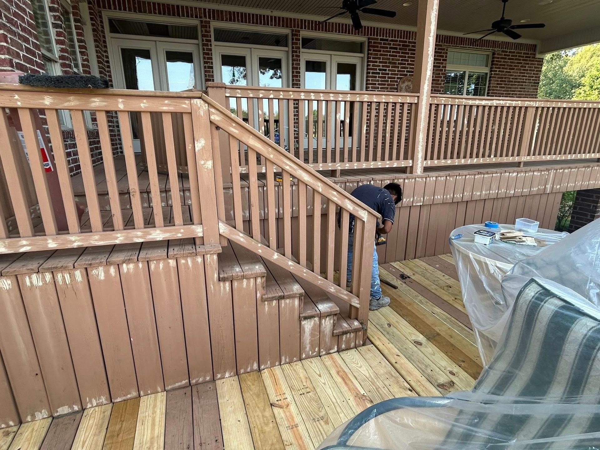 Person painting a wooden deck and staircase outdoors. Brown deck and railing.