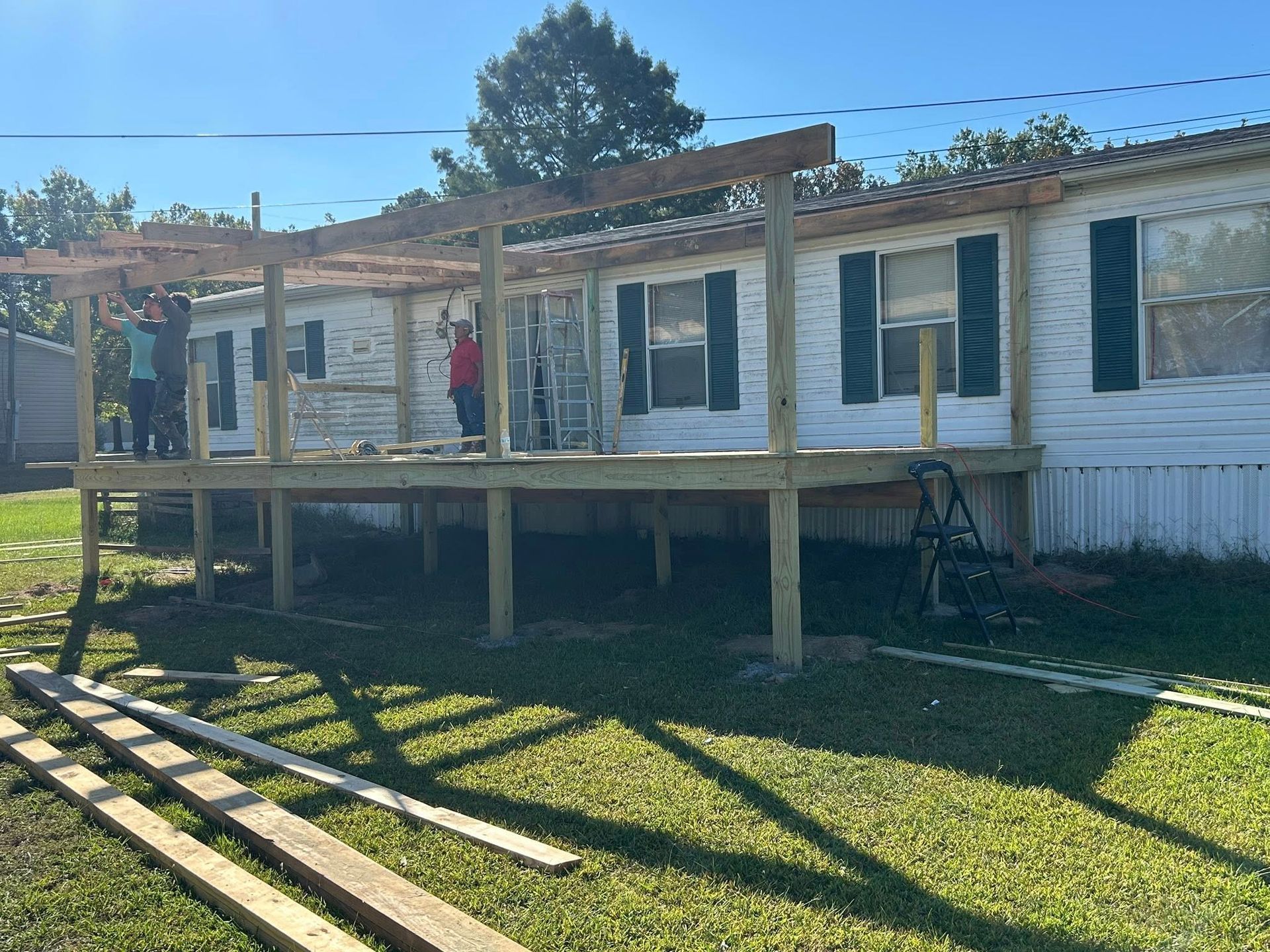 Mobile home with deck under construction; people working on the wooden structure in a grassy yard.