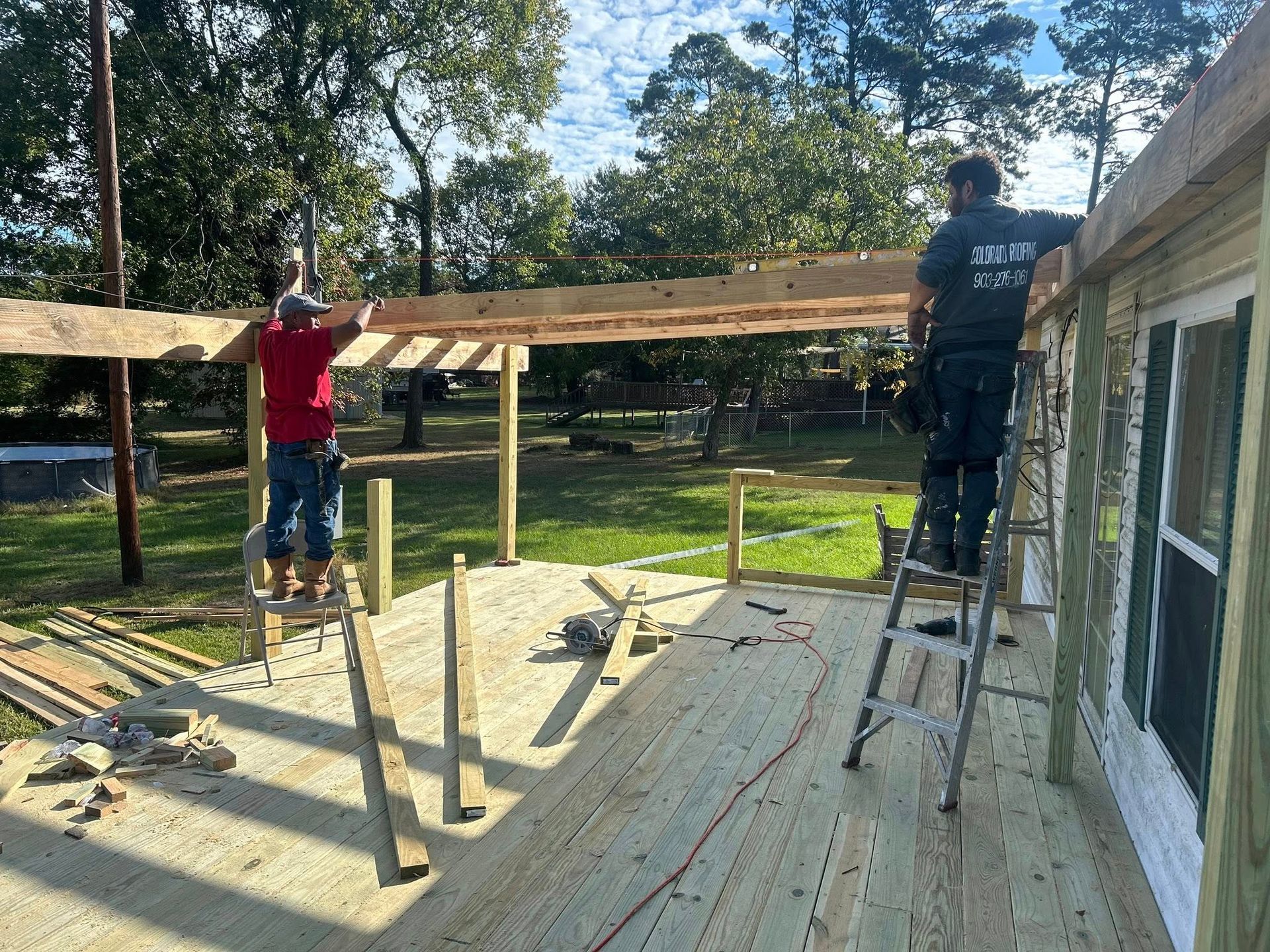 Two people building a wooden deck and pergola on a sunny day.