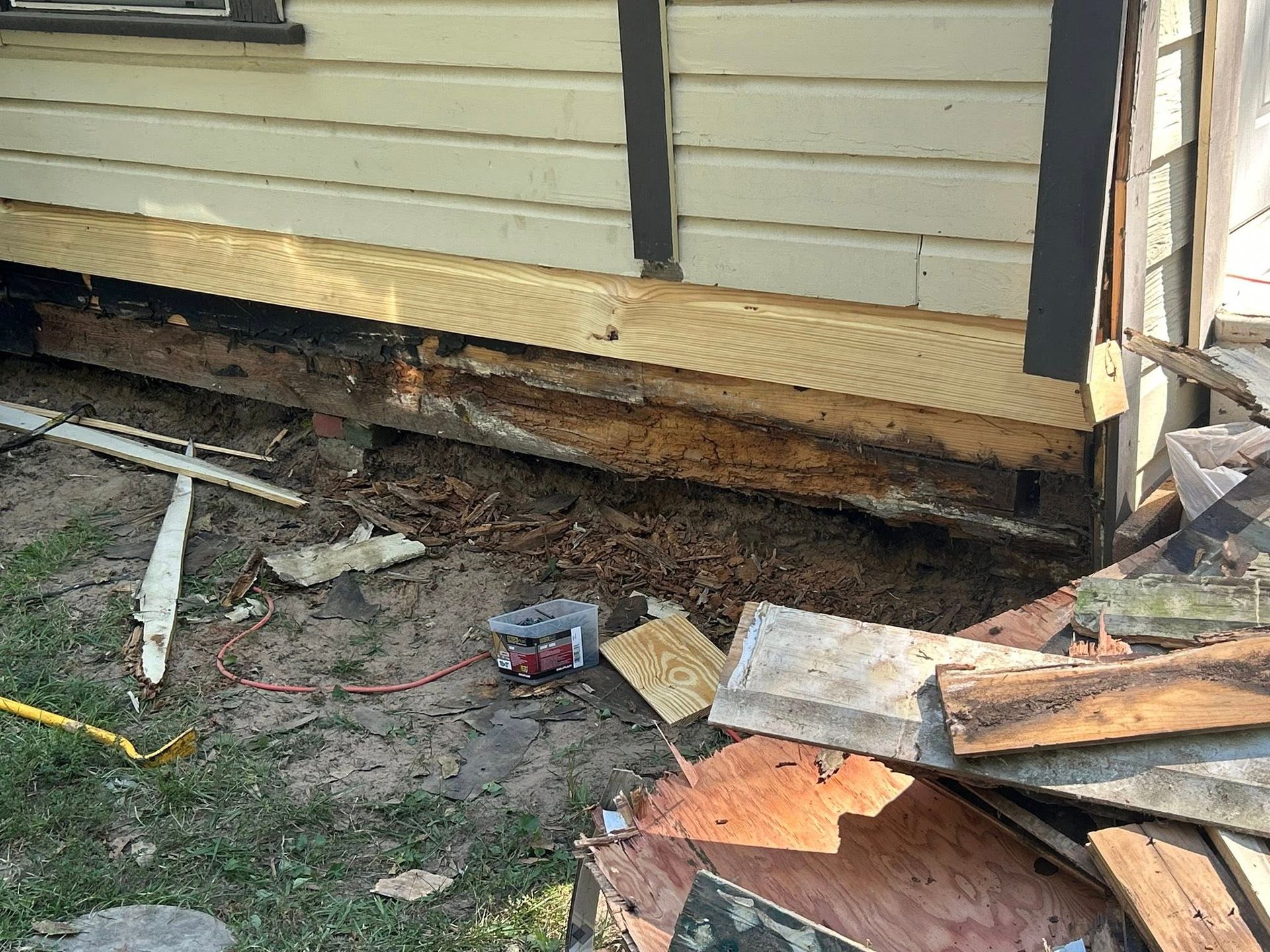 Damaged house foundation being repaired, wood beams exposed, surrounded by debris.