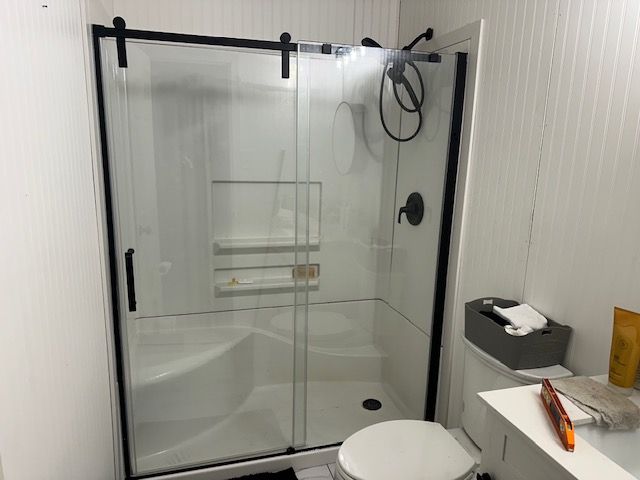 A small white bathroom with a glass sliding door shower, black trim, and a toilet.