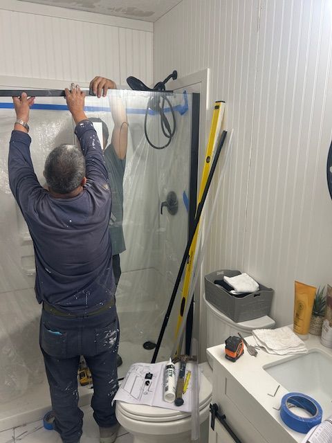 Two people installing a shower door in a bathroom. One person holds the door while the other adjusts the frame.