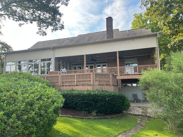 A two-story house with a wooden deck and brick chimney, set on a grassy hill.