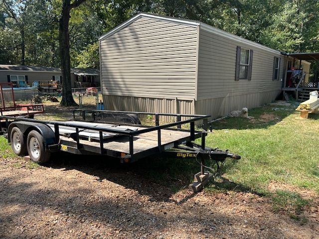 A trailer parked in front of a beige mobile home on a grassy lot.