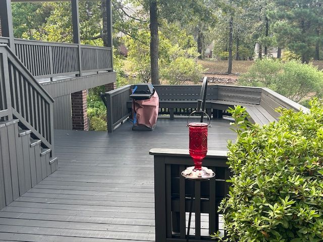 Outdoor deck with gray railings, dark gray flooring, a grill, and a red hummingbird feeder.