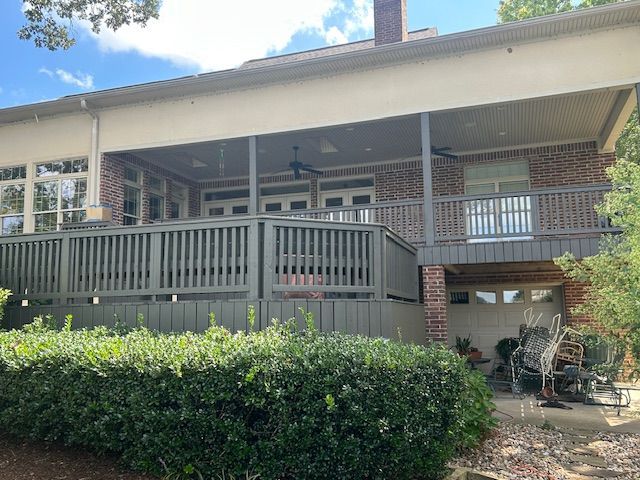 A two-story building with a brick exterior, deck, and green foliage.