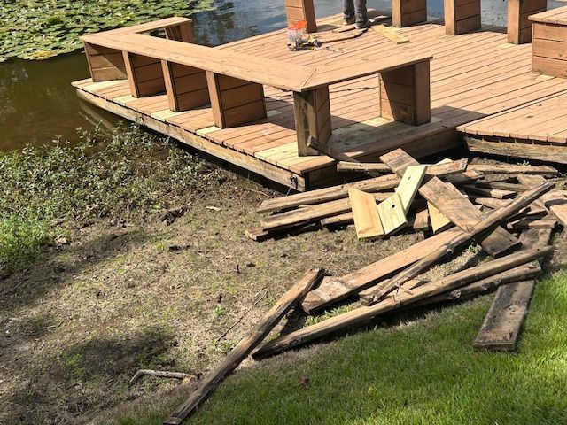 Wooden dock with built-in bench, boards scattered on grass next to water.