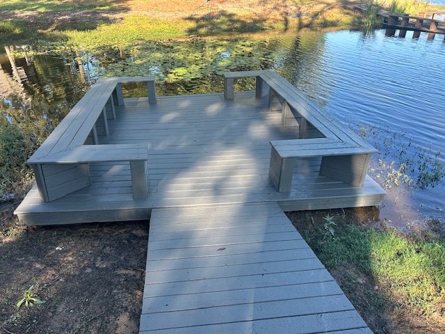Wooden platform with built-in benches, extending into calm water, attached to a wooden walkway.