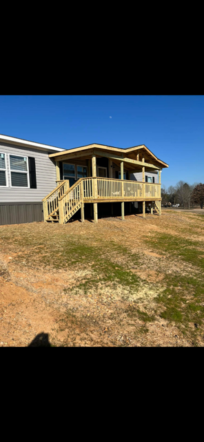 A light gray house with a wooden porch and steps on a grassy brown lot against a blue sky.