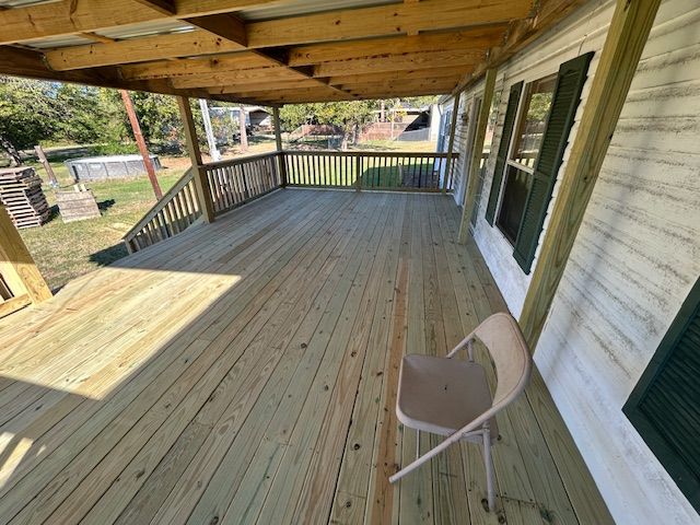 Wooden deck with roof extending from a house. A chair sits on the deck, green shutters on the wall.