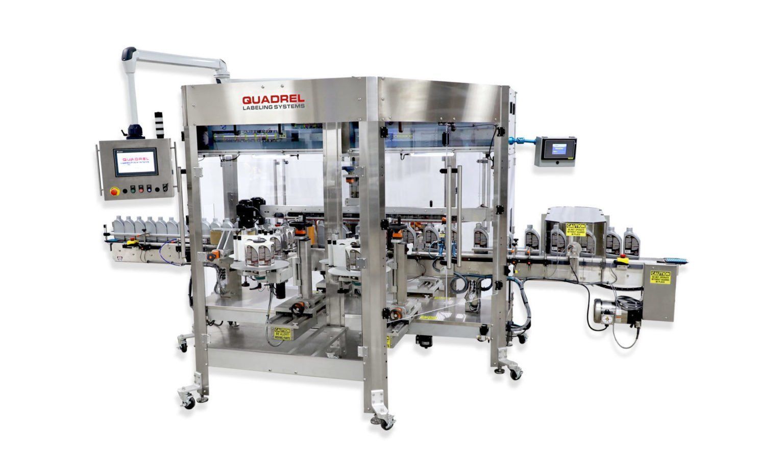 A stainless steel industrial labeling machine on a conveyor system for packaging bottles in a production facility.